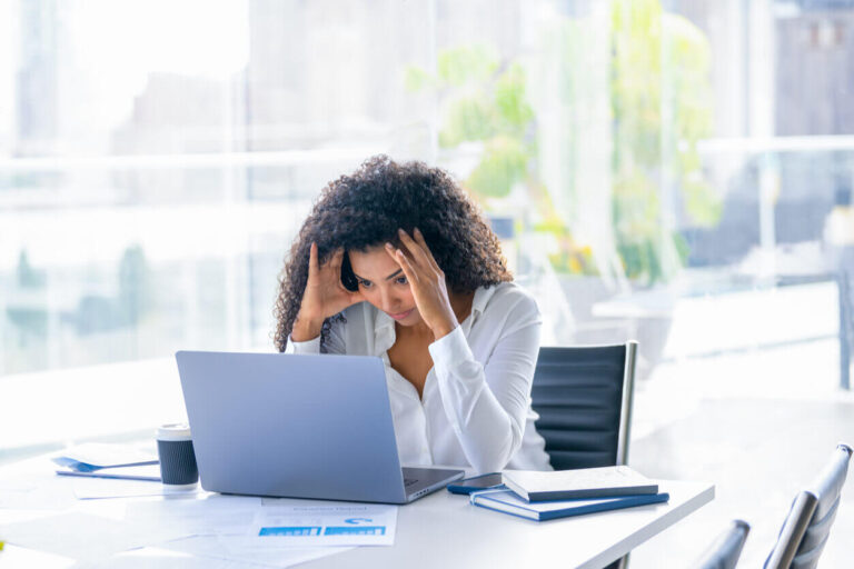 Mulher preocupada no trabalho, demonstrando sinais de estresse e cansaço, possíveis indicativos de doenças ocupacionais invisíveis