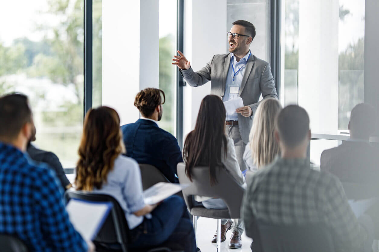 Instrutor conduzindo treinamento para NR1 para um grupo de profissionais em ambiente corporativo, com luz natural e materiais de apoio em mãos.