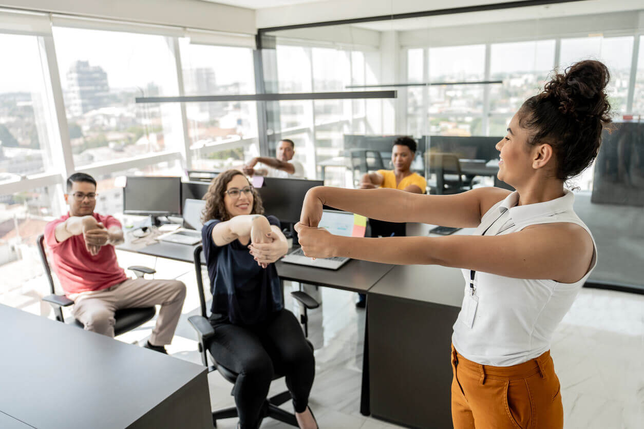 Orientador físico para empresa conduz atividade de alongamento com colaboradores no escritório, promovendo bem-estar físico e emocional no trabalho.