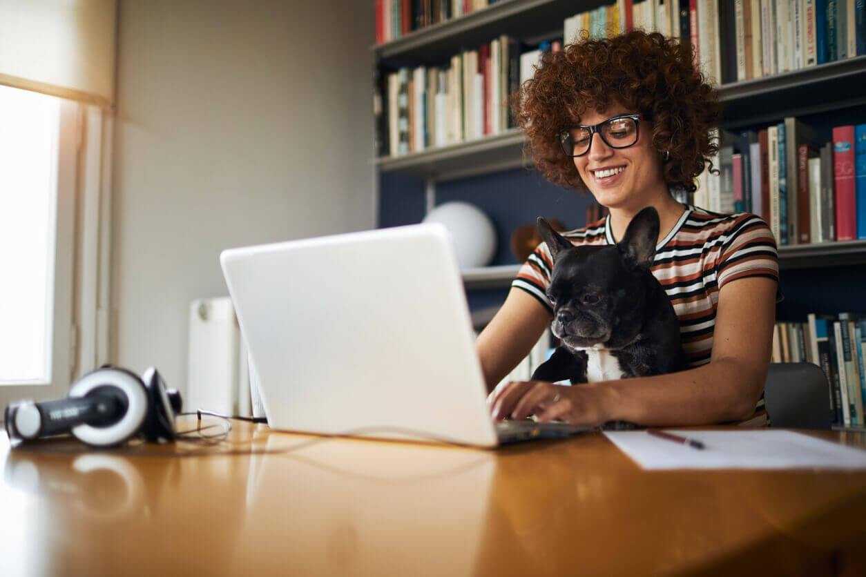 Mulher sorrindo enquanto trabalha em home office com um cachorro no colo, representando a importância de mapear riscos psicossociais no home office para manter o bem-estar.